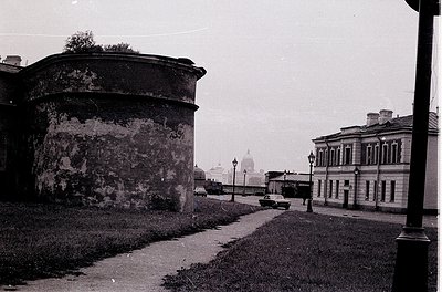 Vintage black-and-white street scene featuring Soviet-era architecture. Prominent round fortress wall with weathered plaster,...