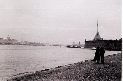 Black-and-white view of St. Petersburg’s Neva River promenade, featuring the Peter and Paul Fortress and its spire in the for...