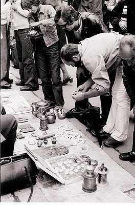 Street-side vintage repair stand with brass and copper tools, featuring a cobbler mending boots while surrounded by antique s...