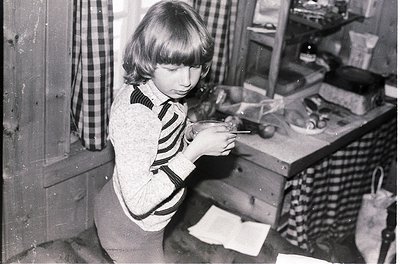 Mid-20th century kitchen scene featuring a child using a manual can opener on a vintage tin can. Wooden cabinetry and checker...