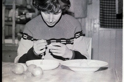 Mid-century kitchen scene featuring a person meticulously peeling a potato with a knife. White plate with peeled potato halve...