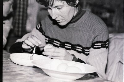 Black-and-white photo of an individual meticulously crafting ceramic pottery using a tool, likely a pottery knife or wire. Th...