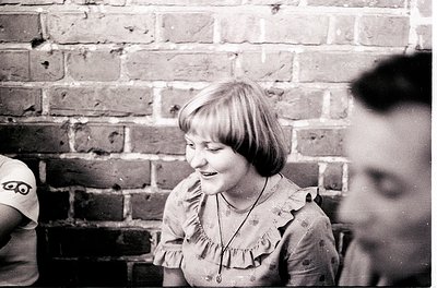Black-and-white candid shot of a young girl in a ruffled blouse, mid-laugh, against a brick wall.