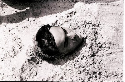 Black-and-white portrait of a person reclining on cracked, textured concrete, likely a rooftop or terrace. The composition hi...
