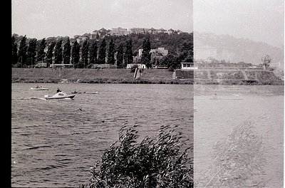 Vintage black-and-white photo of a small motorboat on a calm lake, surrounded by reeds. Mid-20th century lakeside resort with...