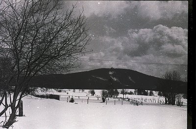 Mid-century black-and-white winter landscape featuring snow-covered fields, barbed-wire fencing, and a distant hilltop struct...