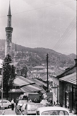 Vintage black-and-white street scene featuring a prominent Ottoman-style minaret and dense urban rooftops. Mid-20th century c...