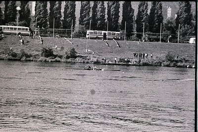 Vintage black-and-white shot of a lakeside scene with mid-20th century buses parked on grassy embankment. People swim, wade, ...