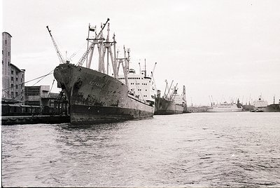 Mid-20th century industrial port scene featuring a rusted cargo ship ("Sofia") docked alongside modernist concrete warehouses...