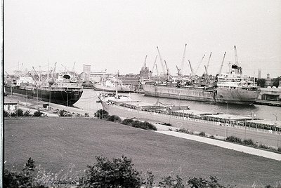 Black-and-white port scene featuring mid-20th century passenger ships docked alongside cranes and industrial infrastructure. ...