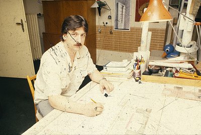 Mid-century artist engrossed in abstract painting, seated at a cluttered wooden table with paint-splattered clothing. Surroun...
