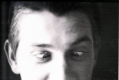 Close-up portrait of a man with short, neatly combed hair, captured in black-and-white. The grainy texture and lighting sugge...