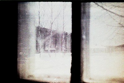 Vintage sepia-toned photo of a foggy, snow-covered urban scene. Bare trees frame a partially obscured multi-story building wi...