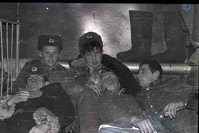 Vintage black-and-white photo of three uniformed men in a dimly lit, industrial setting—likely a train or ship cabin. Left: s...
