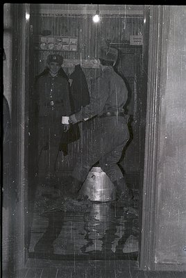 Two uniformed soldiers in heavy winter gear stand in a flooded subway entrance, 1960s-70s Eastern Bloc. One holds a helmet, t...