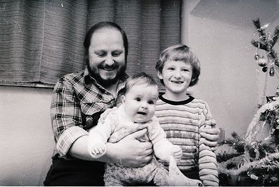 Black-and-white family portrait featuring a man in a plaid shirt holding a baby, with a smiling child beside him. Decorated C...