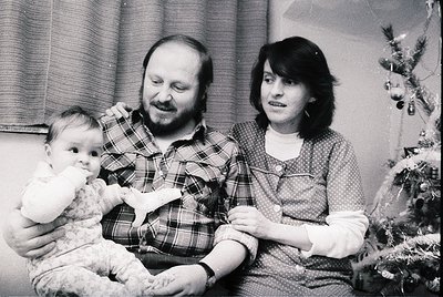A black-and-white family portrait from the **1970s–1980s**, featuring a man in a plaid shirt, a woman in a patterned blouse, ...