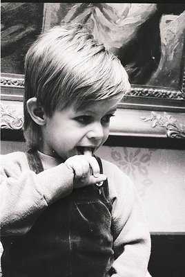 Young child in vintage sweater brushing teeth indoors, framed classical painting in background. Mid-20th century domestic sce...