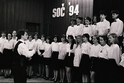 Young choir in formal attire performs on stage, 1994 Soči event. Uniforms feature white blouses, bow ties, and dark vests. St...