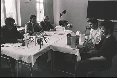 Mid-century conference room featuring five men in formal attire (suits, ties) reviewing architectural models and documents, 1...