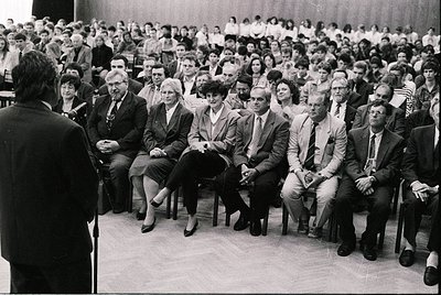 Black-and-white photo of a formal indoor lecture or conference, likely mid-20th century. Audience seated in tiered rows, men ...