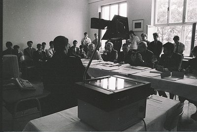 Mid-20th century conference room with vintage projector and attendees in formal attire. Large screen reflects light, suggesti...