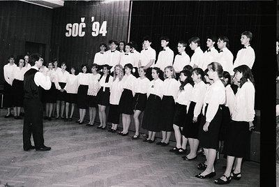 School choir rehearsal, 1994, likely Eastern Europe. Uniformed students in white blouses and dark skirts/shorts stand in rows...