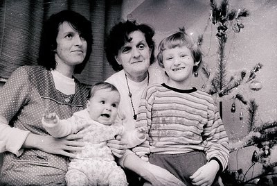 Family portrait from the 1960s–1970s, featuring three generations: a woman holding a baby, a seated elderly woman, and a youn...