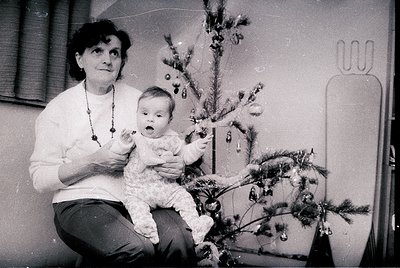 A black-and-white snapshot from the mid-20th century (likely 1950s–1970s) captures a tender holiday moment. An adult holds a ...