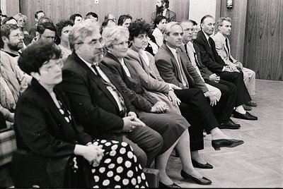 A formal indoor gathering of adults seated in rows, likely a conference or meeting in the 1970s–1980s. Wood-paneled walls and...