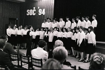 Youth choir performing in a Soviet-era indoor venue, 1970s–1980s. Uniform white shirts with black vests, led by a conductor. ...
