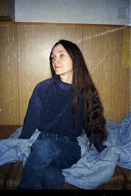 Vintage portrait of a person with long, straight hair in a ribbed sweater and high-waisted jeans, seated on a bed with a stri...