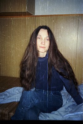 Portrait of a person with long, straight hair in a vintage indoor setting. The individual wears a dark blue ribbed sweater an...