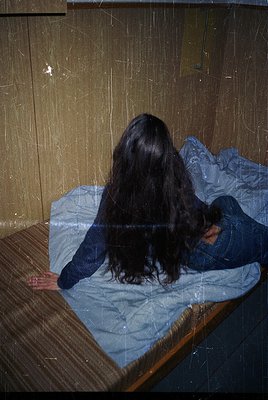 Vintage-style portrait of a person lying on a wooden bed with a blue blanket, back to camera. Warm lighting and slight grain ...