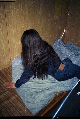 Vintage-style portrait of a person lying on a wooden bed with a faded blue blanket, wearing a dark sweater and distressed jea...