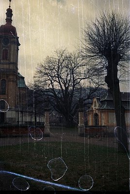 Vintage photograph of a historic European church tower framed by rain-streaked glass. Barren trees and classical architecture...