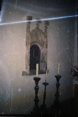 Gothic-style stone window niche with lattice tracery, flanked by two ornate candle holders. Interior architectural detail, li...