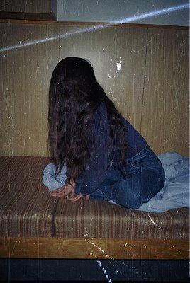 Vintage-style portrait of a person seated on a wooden bench, back to camera, with long hair cascading over denim jacket sleev...