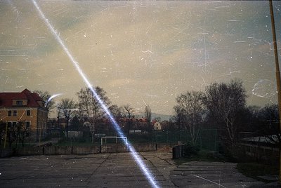 Vintage urban scene through scratched glass, revealing a residential area with Soviet-era architecture. Yellow brick apartmen...