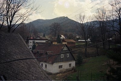 Rural village scene featuring a two-story timber-framed house with a steep gable roof, surrounded by leafless trees and rolli...