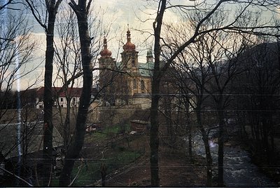 Baroque-style church with twin golden domes and green-roofed spires framed by bare winter trees. Overcast sky enhances muted ...