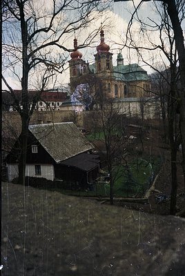 Baroque-style church with twin domed towers and intricate façade framed by bare winter trees. Foreground shows rustic cottage...