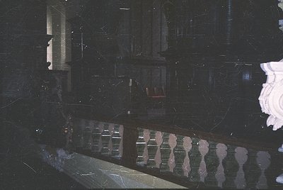 Vintage black-and-white photo of a grand, dimly lit interior staircase with ornate wrought-iron railings and marble steps. Re...