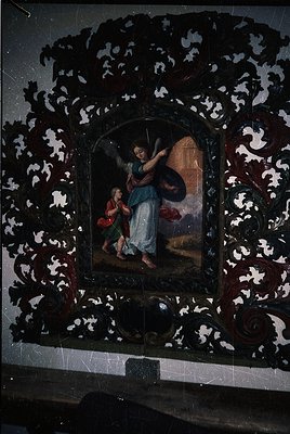 Baroque-style religious icon framed in intricately carved wood with floral and scroll motifs. Central painting depicts an ang...