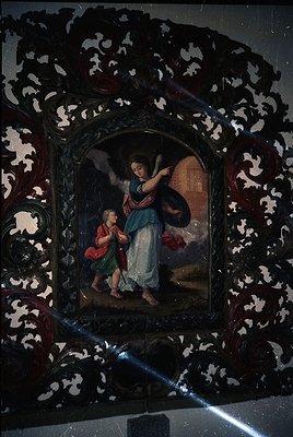 Baroque-style religious painting framed in ornate damask pattern, depicting an angelic figure (blue robe, wings) presenting a...