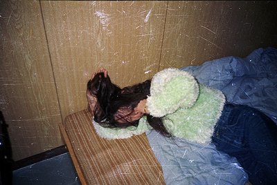 Vintage interior shot featuring a child resting on a wooden bench with a green knitted blanket. Plain wall and plastic sheeti...