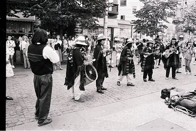 Street performance featuring traditional musicians in folk attire, likely Eastern European. Group plays accordion, drums, and...