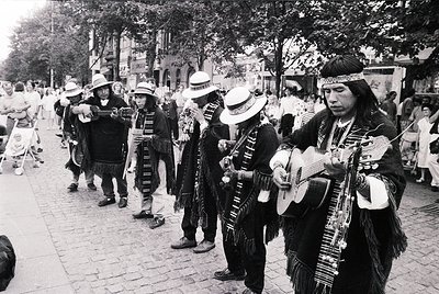 Street performance featuring traditional Andean musicians in elaborate, fringed ponchos and wide-brimmed hats, playing acoust...