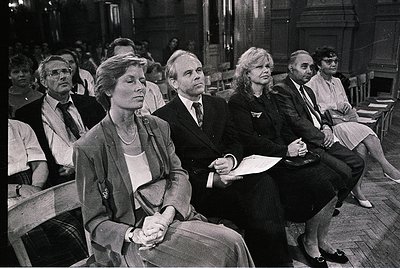 Black-and-white interior shot of seated attendees in a formal event, likely a 1970s–1980s conference or trial. Wooden pews an...