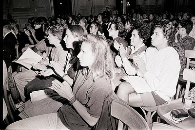 Black-and-white photo of a packed lecture hall, likely from the 1960s–1970s. Attendees, mostly young adults, sit attentively ...
